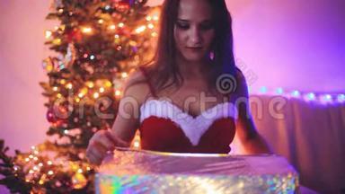 年轻快乐的女人打开神奇的<strong>圣诞</strong>礼物，手持闪亮的<strong>灯光</strong>。 女孩坐在<strong>圣诞</strong>树旁边装饰